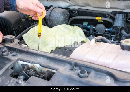 Nahaufnahme: Automechaniker, der Motorölmessstab von Hand zieht, um den Motorölstand im Motorraum zu prüfen. Stockfoto