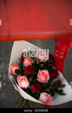 Strauß aus roten und rosa Rosen, der unter dem roten Tisch steht Stockfoto