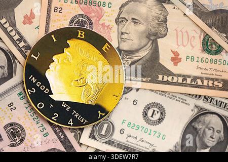 KIEW, UKRAINE - 13. DEZEMBER 2025 Trump Goldmünze auf große Menge von US-Dollar-Geldscheine Banknoten aus nächster Nähe Stockfoto