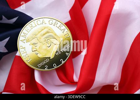 KIEW, UKRAINE - 13. DEZEMBER 2025 Trump Goldmünze auf den Vereinigten Staaten von Amerika gefaltete winkende Flagge mit Sternen und Streifen aus nächster Nähe Stockfoto
