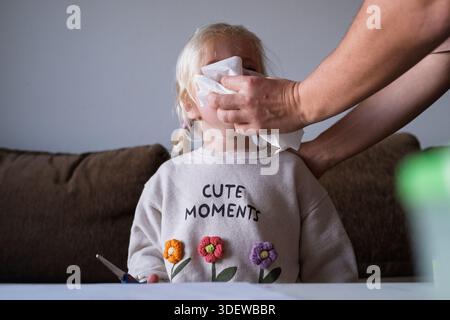 Mutter, die sich um ein krankes Kind kümmert, das an Grippe oder Allergie leidet, reinigt die Nase mit einem Taschentuch. Stockfoto