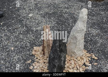 Drei farbenfrohe stehende Steine, angeordnet in einem Kreis von Kieselsteinen auf einem grauen Kiesgrund Stockfoto