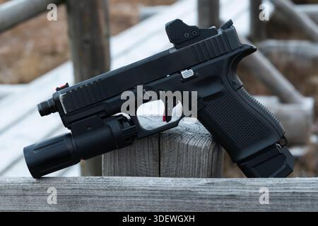 Moderne halbautomatische taktische Pistole mit rotem Punkt und Taschenlampenbefestigung auf einem Holzzaun im Freien. Stockfoto