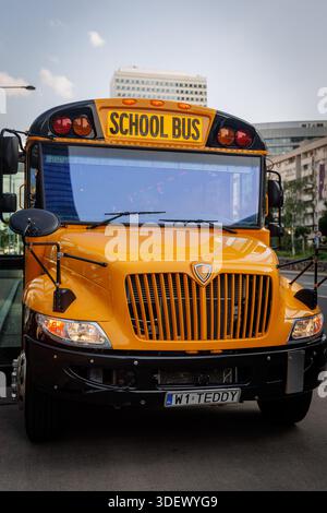Vorderansicht eines gelben Schulbusses auf einer Stadtstraße mit hohen Gebäuden im Hintergrund. Stockfoto