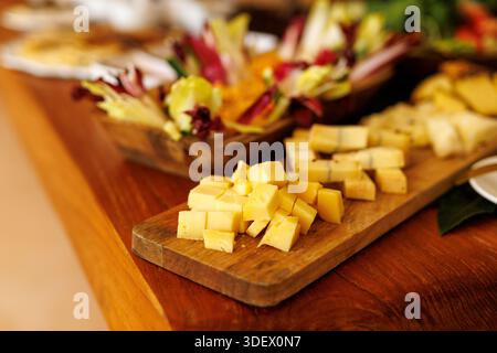 Kleine Würfel mit gelbem Käse auf einem Holzbrett mit verschiedenen Vorspeisen im Hintergrund. Stockfoto