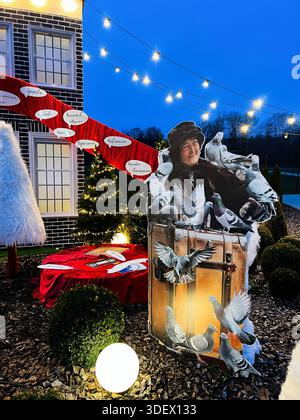 Chodakhkiv, Ukraine - 29. November 2025: Festliche Outdoor-Szene mit lebensgroßem Ausschnitt, Tauben, Reisekoffer, Lichtern und Urlaubsdeco Stockfoto