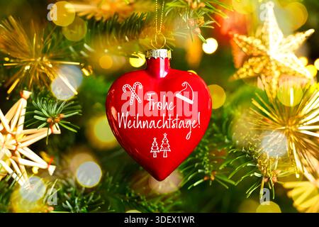 Weihnachtskugel in Herzform mit der Inschrift Frohe Weihnachten hängt an einem Weihnachtsbaum, Fotomontage Stockfoto