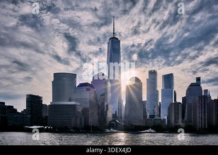 Die legendäre Skyline von New York City verfügt über hoch aufragende Wolkenkratzer, darunter das prominente One World Trade Center, das von dramatischen Sonnenlichtfiltern umgeben ist Stockfoto