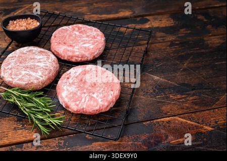 Gefrorene Fleischpasteten, bereit zum Grillen, Forcemeat von Schwein und Rindfleisch für Burger. Hölzerner Hintergrund. Draufsicht. Stockfoto