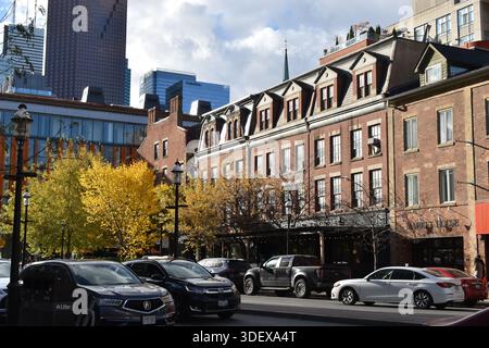 Historische Backsteingebäude und Herbstbäume entlang einer belebten Downtown Street in Toronto, Kanada, mit modernen Wolkenkratzern im Hintergrund und Parkplätzen Stockfoto