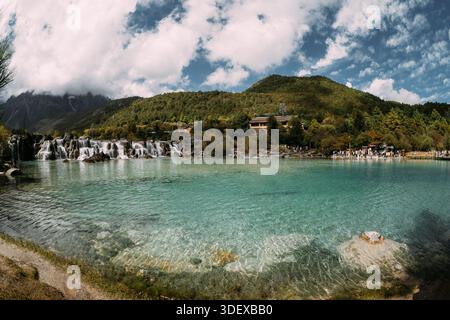 Der weite Panoramablick umfasst den weiten türkisfarbenen See, kaskadierende Wasserfälle und dichte bewaldete Hänge im Blue Moon Valley in der Nähe von Lijiang. Klarwasser r Stockfoto