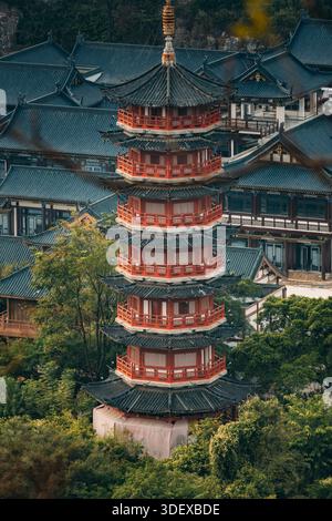 Blick aus der Nähe auf die mehrstufige rote Pagode, die über den Dächern des Tempelkomplexes in Guilin, China, ragt. Komplizierte Holzbalkone, geschwungene Traufe und üppige Umgebung Stockfoto