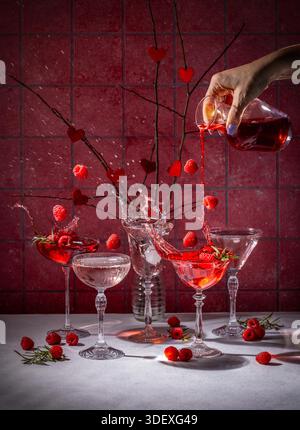 Weibliche Hand gießt roten Cocktail in Vintage-Kristallgläser mit Himbeerplätschern und schafft eine romantische, festliche Szene mit Festlichkeiten und eleganten Getränken zum valentinstag Stockfoto