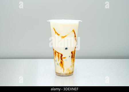 Eine wackelige, weiße Schicht Kokosgelee bedeckt die untere Hälfte eines Glases, gekrönt mit hellbraunem Milchtee und goldenen Tapiokaperlen Stockfoto