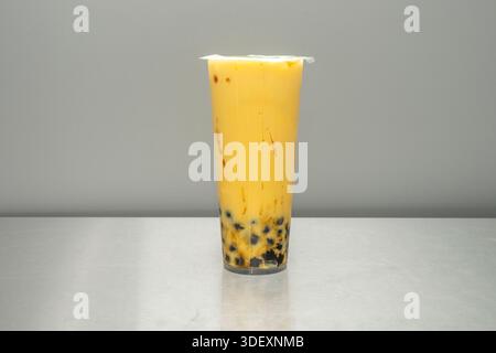 Ein Glas Passionsfrucht-Bubble-Tee mit zahlreichen schwarzen Samen, die in einer durchscheinenden gelben Flüssigkeit aufgehängt sind, und einem breiten Strohhalm, der zum Einführen bereit ist Stockfoto