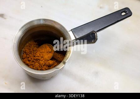 Traditioneller griechischer gemahlener Kaffee in einem kleinen Metall-Briki, auf einer sauberen weißen Marmorarbeitsfläche, bereit zum Brühen. Stockfoto