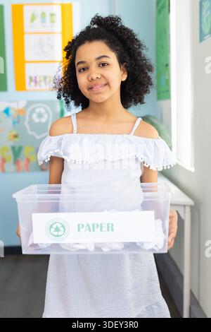 Afroamerikanischer Teenager, der in der Klasse steht und einen PAPIERKORB mit zerknittertem Papier in einem gerafften Kleid hält Stockfoto