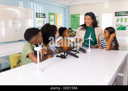 Afroamerikanischer Lehrer im grünen Hemd, der fünf Kinder führt, die Windräder mit Tablets testen Stockfoto