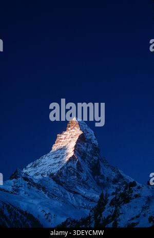 Die Sonne geht mit goldenem Glanz auf und trifft auf den Gipfel des Matterhorns, der im Winter über dem schneebedeckten Bergdorf Zermatt in der Schweiz aufragt und eine dramatische Bergkulisse, eiskalte Gipfel und die berühmte Skyline eines der berühmtesten Reiseziele der Alpen bietet. Stockfoto