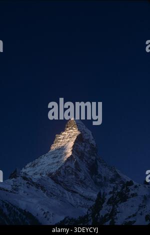 Die Sonne geht mit goldenem Glanz auf und trifft auf den Gipfel des Matterhorns, der im Winter über dem schneebedeckten Bergdorf Zermatt in der Schweiz aufragt und eine dramatische Bergkulisse, eiskalte Gipfel und die berühmte Skyline eines der berühmtesten Reiseziele der Alpen bietet. Stockfoto