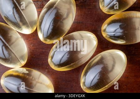 Makroaufnahme gelber flüssiger Vitaminkapseln auf braunem Holzhintergrund. Konzept von Nahrungsergänzungsmitteln, täglicher Gesundheitsversorgung und Wellness-Routine. Stockfoto