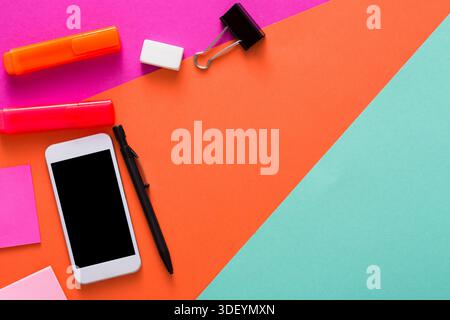 Farbenfrohe Schreibwaren und Smartphone im lebendigen Office Workspace angeordnet Stockfoto