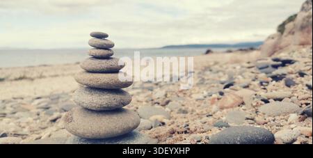 Ein ausgewogener Stapel glatter Steine an einem ruhigen Kiesstrand, der Ruhe, Achtsamkeit und Harmonie am Meer symbolisiert Stockfoto