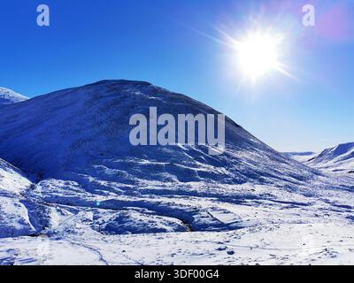 Schneebedeckte schottische Highlands in Glenshee, umgeben von weißen Berggipfeln und vor einem auffälligen tiefblauen Winterhimmel Stockfoto