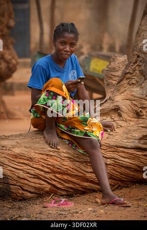 Porträt eines lokalen madagassischen Mädchens, das auf einem Baumstamm auf dem Markt sitzt, Belo Tstiribhina, Madagaskar. Die lokale Bevölkerung in und um Belo Tsiribihina gehört vor allem der Sakalava-Volksgruppe an. Der Markt in Belo Tsiribihina, auch bekannt als Marché Communal, ist ein pulsierendes Zentrum des lokalen Handels und des täglichen Lebens in der Region Menabe im Westen Madagaskars. Der Markt ist ein zentraler Treffpunkt für die Gemeinde Stockfoto