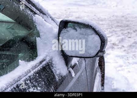 Gefrorener Autoflügelspiegel, der an einem kalten Wintermorgen unter einer dicken Schicht flauschigen Schnees vergraben wurde, zeigt die Notwendigkeit der Fahrzeugreinigung und -Wartung Stockfoto