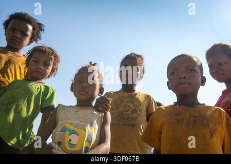 Eine Menge neugieriger madagassischer Kinder versammelt sich. Madiokely, Madagaskar. Mehr als zwei Drittel der madagassischen Kinder leiden in mindestens zwei wesentlichen Dimensionen des Wohlbefindens, wie Ernährung, Gesundheit oder Bildung, unter materieller Benachteiligung. Obwohl der Besuch der Grundschule häufig ist, schließt nur jedes dritte Kind tatsächlich die Grundschulbildung ab. In vielen ländlichen Gebieten werden Kinder aus der Schule gezogen, um zum Haushaltseinkommen oder zu Aufgaben beizutragen, wie Wasserholen oder Glimmerabbau. Stockfoto