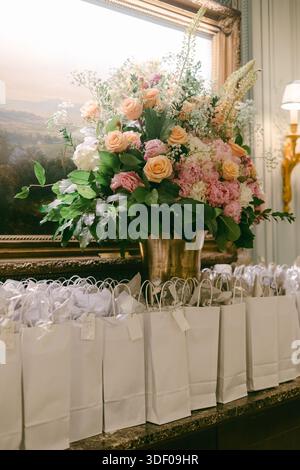 Ein großes Blumenarrangement steht auf einem Tisch neben vielen kleinen weißen Geschenktüten für eine besondere Veranstaltung. Stockfoto