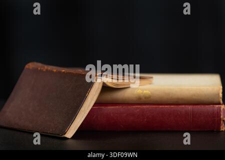 Ein Stapel alter Bücher mit einem braunen, ledergebundenen Buch auf einer dunklen Oberfläche vor schwarzem Hintergrund. Stockfoto