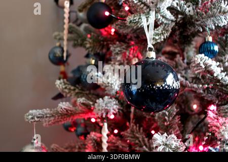 Weihnachtsbaum mit Schnee und blauen und silbernen Kugeln und rosa Lichtern neben einem Bücherregal mit Nahfokus (linke Seite) Stockfoto