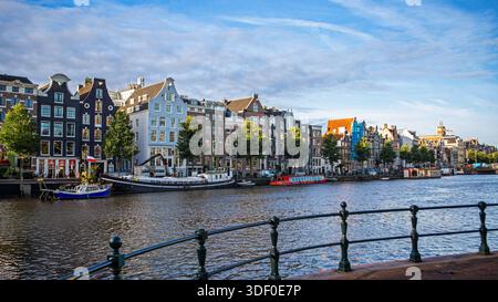 Farbenfrohe Grachtenhäuser und Boote in Amsterdam. Malerischer Blick auf traditionelle holländische Grachtenhäuser entlang einer Uferpromenade in Amsterdam, mit Booten und Stockfoto