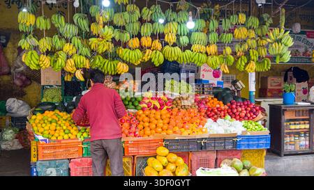 Lebendige Auswahl an frischem Obst an einem Marktstand mit einem Händler, mit farbenfrohen Produkten und einem lebhaften Markt. Stockfoto