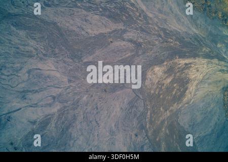 Faszinierende Aussicht von oben auf einen dunklen gefrorenen See mit schwirrenden weißen Schneemustern. Das tiefblaue Eis mit Frostdetails schafft eine einzigartige abstrakte Textur, die an luxuriösen Marmorstein, fließende Acrylkunst oder einen Tiefraumnebel erinnert. Stockfoto