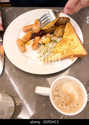 Teller mit Mini-Würstchen, Toast, gerösteten Kartoffeln, Reis und Gemüse serviert mit einer Tasse Kaffee auf einem Marmortisch malaysia Stockfoto