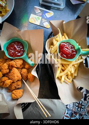 Knusprige Hähnchennuggets und Pommes frites serviert mit Ketchup in papierbeschichteten Körben auf einem dunklen Tisch in malaysia Stockfoto