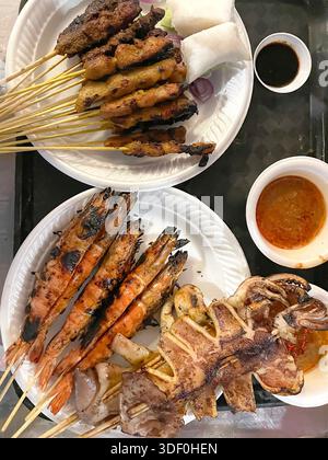 Gegrillte Meeresfrüchte- und Fleischspieße auf Papiertellern mit eintauchenden Saucen in einem Street Food Stall oder einem zwanglosen Restaurant singapur asia Stockfoto