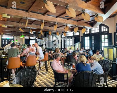 Die Long Bar im historischen Raffles Hotel in Singapur bietet Gästen Speisen und Trinken singapur, Cocktails, Deckenventilatoren und gemusterte Fliesenböden Stockfoto