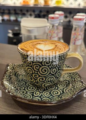 Cappuccino mit herzförmiger Latte Art, serviert in einer Tasse mit Spiralmuster - ein perfektes Café Momen Stockfoto