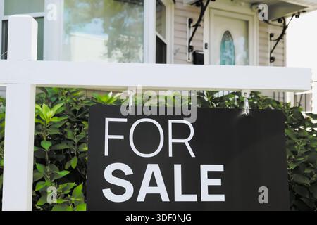 Zu verkaufen Immobilien-Schild Nahaufnahme vor einem kleinen Vorstadthaus Stockfoto