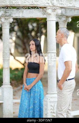 Ein Mann und eine Frau stehen vor einem weißen Torbogen. Die Frau trägt ein schwarzes Oberteil und einen blauen Rock. Der Mann trägt ein weißes Hemd und Khak Stockfoto