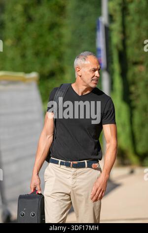 Ein Mann, der ein schwarzes Hemd und eine khakifarbene Hose trägt, läuft mit einer Aktentasche in der Hand einen Bürgersteig hinunter Stockfoto
