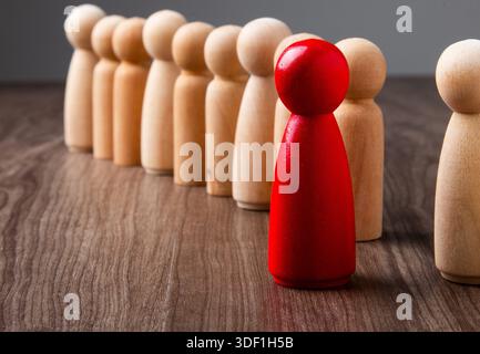 Rote Stangenfigur, die sich von einer Linie aus natürlichen Holzstiften auf einer Holzoberfläche abhebt Stockfoto