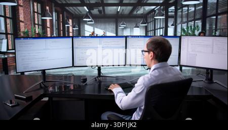 Technisch Versierter Mann, Der Mehrere Bildschirme In Geschäftiger Büroumgebung Jongliert Stockfoto