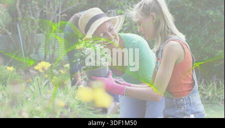 Kniende Frau mit Kind, die Pflanzen im Garten präsentiert, mit Strohhut, rosa Handschuhen, Jeansanzügen Stockfoto