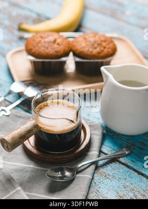 Eine Tasse heißer schwarzer Kaffee, Espresso, frisch gebackene Muffins. Bananen-Cupcake-Nahaufnahme als Dessert für die Kaffeepause. Draufsicht. Erfrischend am Morgen und am Tag Stockfoto