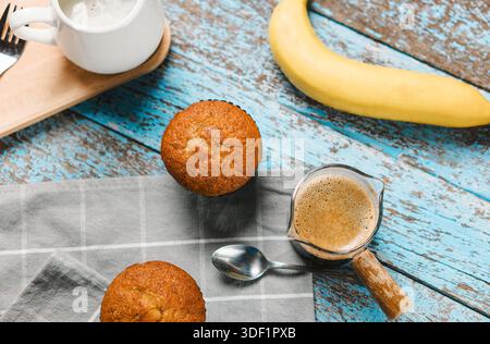 Eine Tasse heißer schwarzer Kaffee, Espresso, frisch gebackene Muffins. Bananen-Cupcake-Nahaufnahme als Dessert für die Kaffeepause. Draufsicht. Erfrischend am Morgen und am Tag Stockfoto